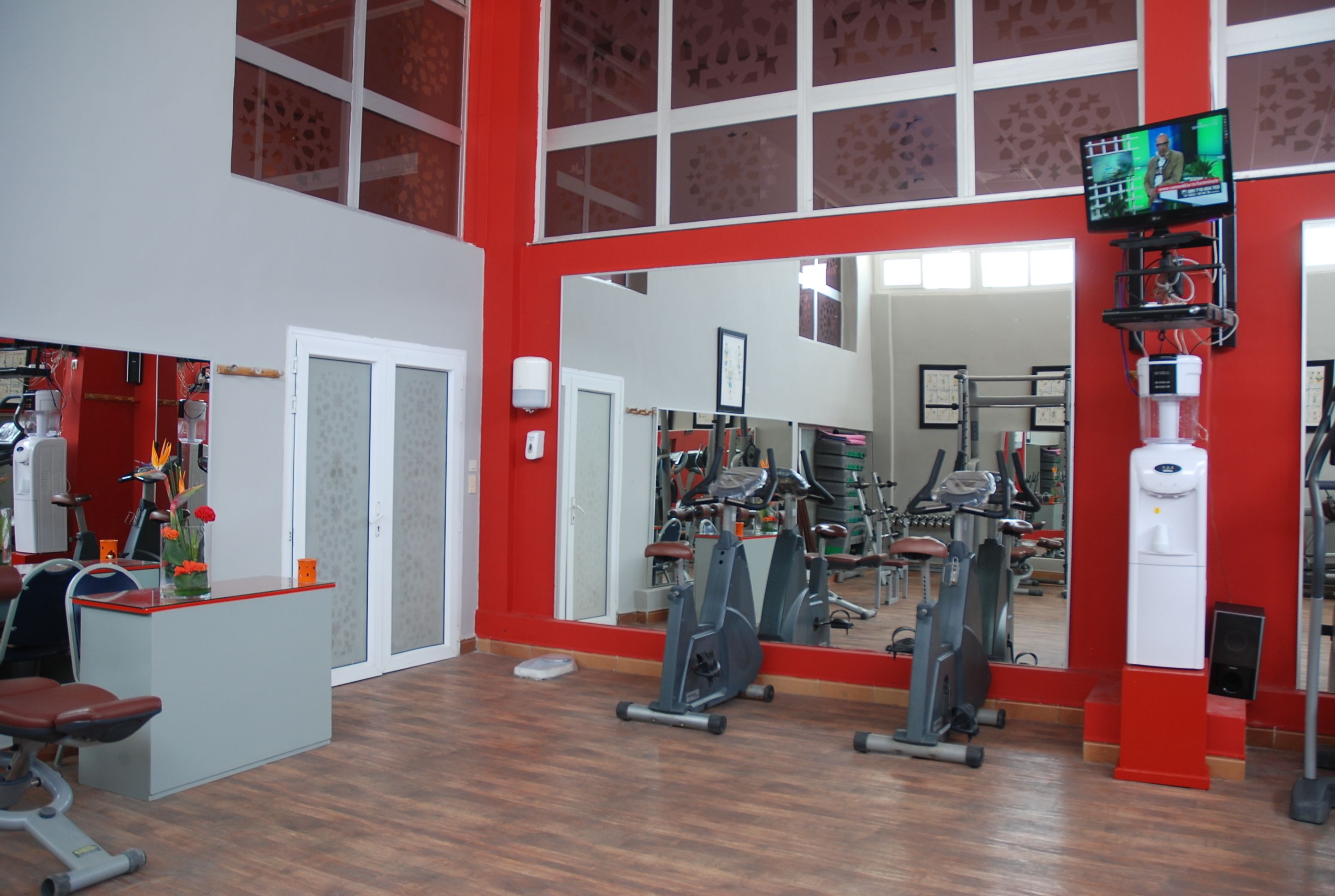 Un gimnasio con equipo de ejercicio, una recepción y un espejo grande que refleja el equipo.