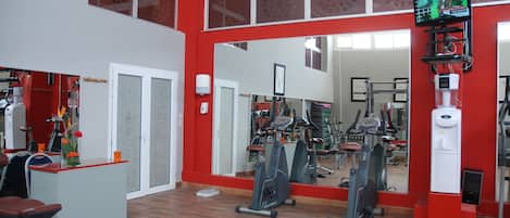 Un gimnasio con equipo de ejercicio, una recepción y un espejo grande que refleja el equipo.