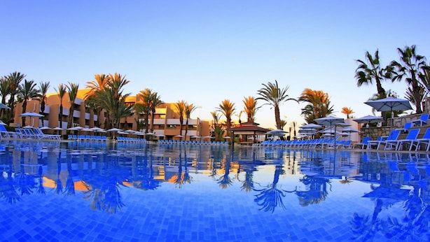 A swimming pool with blue chairs and umbrellas, surrounded by palm trees and hotel buildings. - Dunes d'Or Ocean Club (Agadir)