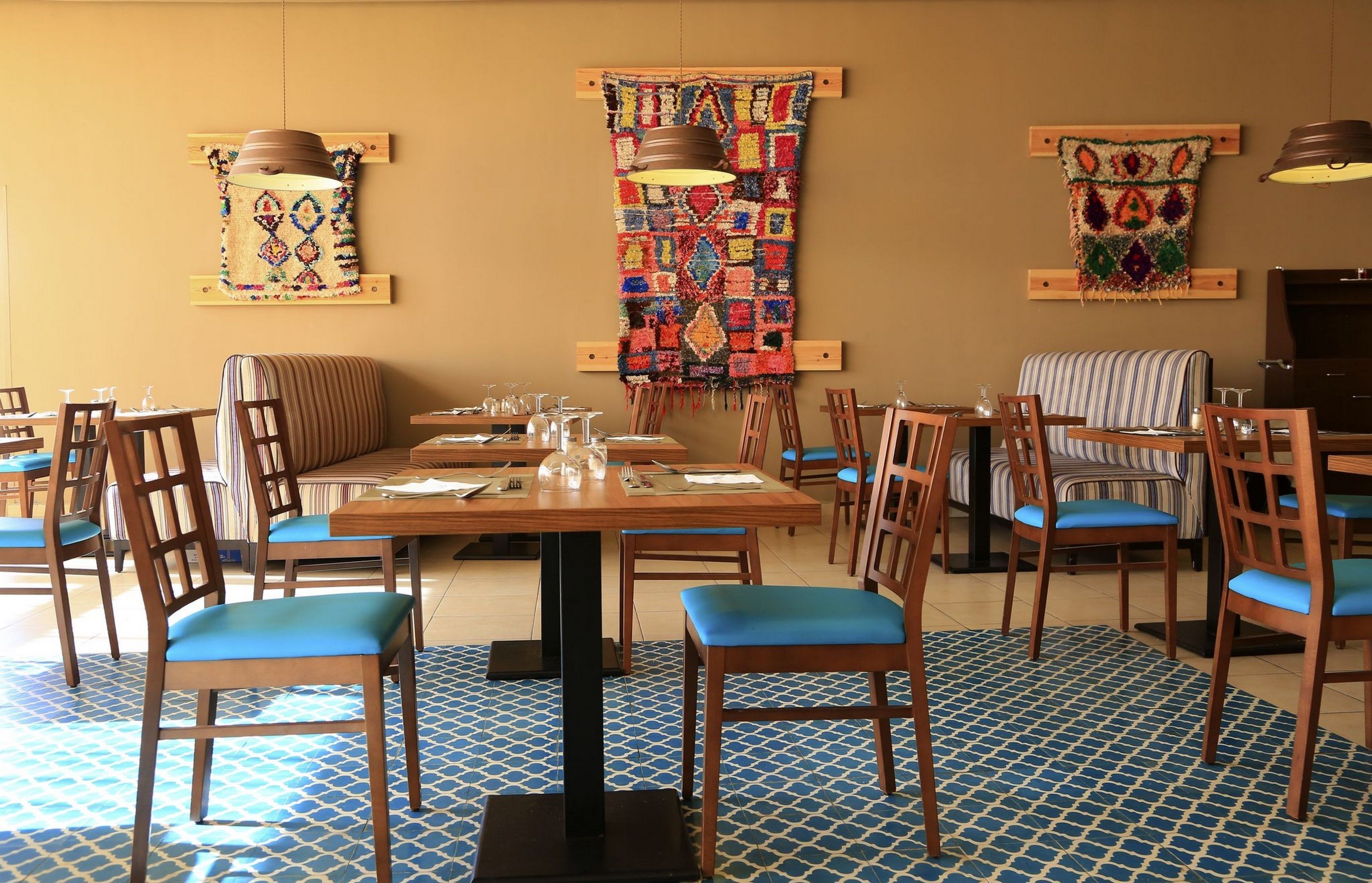 A restaurant with wooden tables and chairs, a patterned wall hanging, and a blue patterned floor.