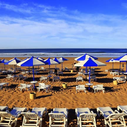 A beach with rows of white lounge chairs and blue and white umbrellas.