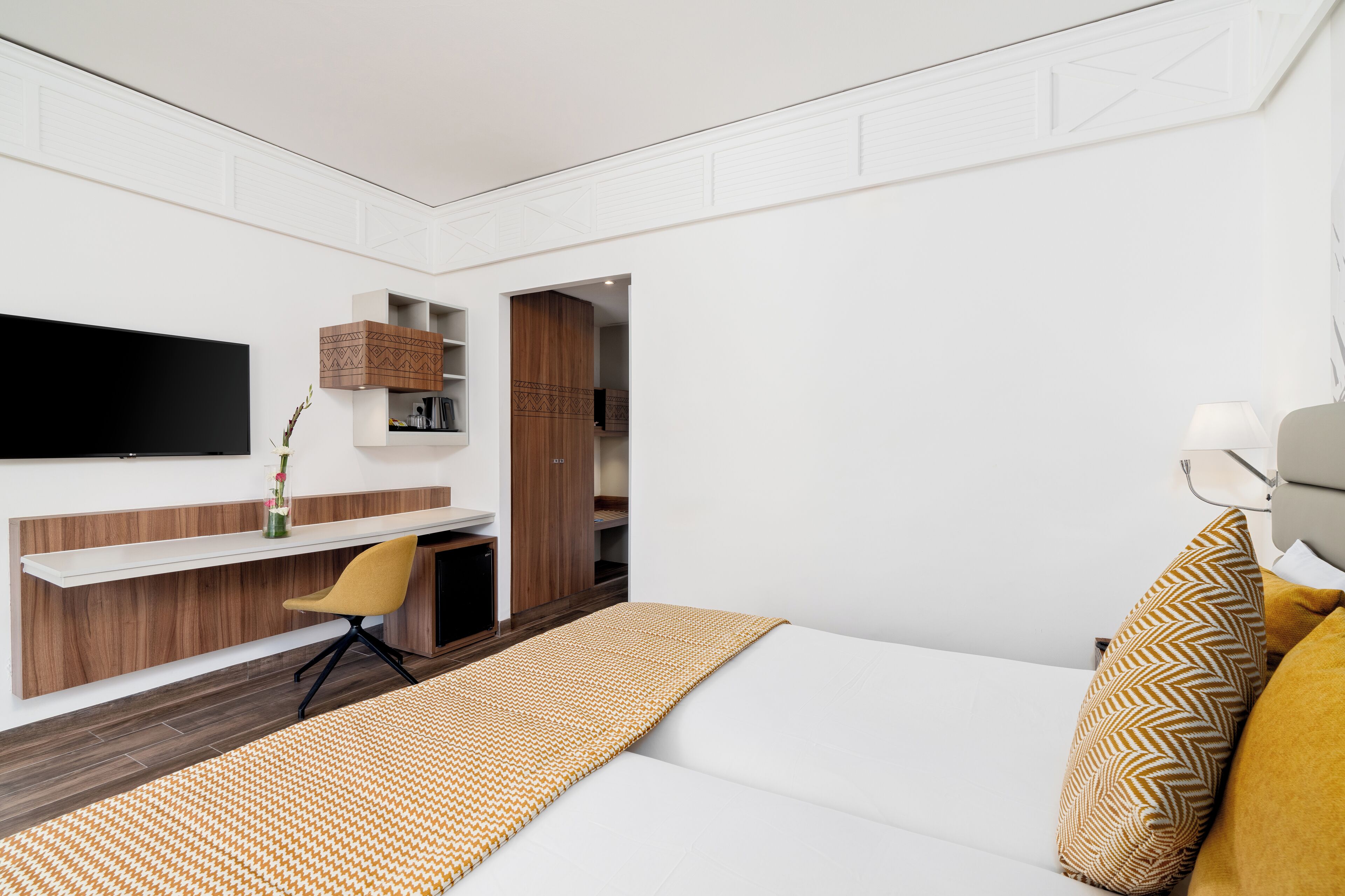 A modern hotel room with a bed, a desk, a chair, and a TV mounted on the wall.