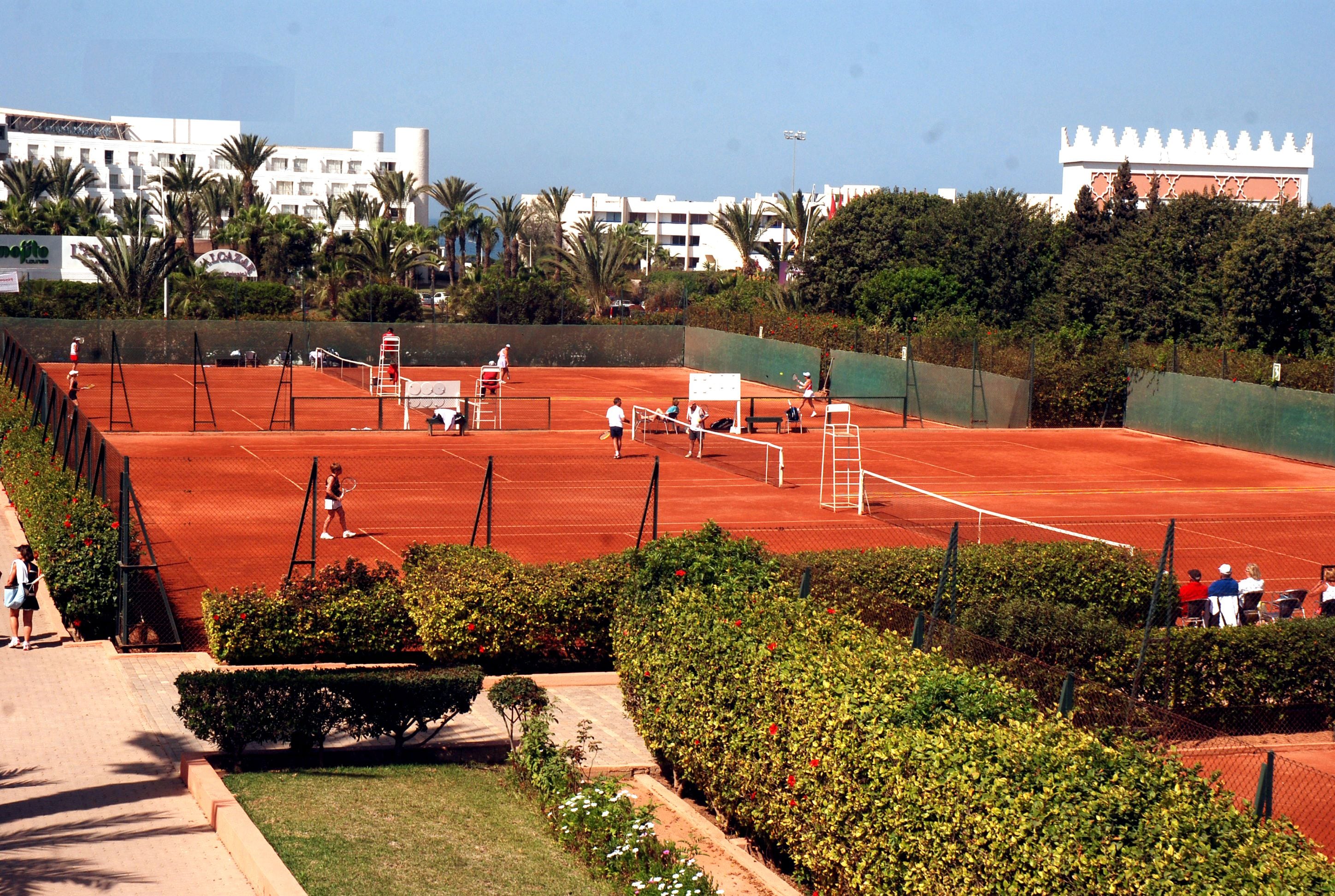 A tennis court surrounded by greenery and buildings.