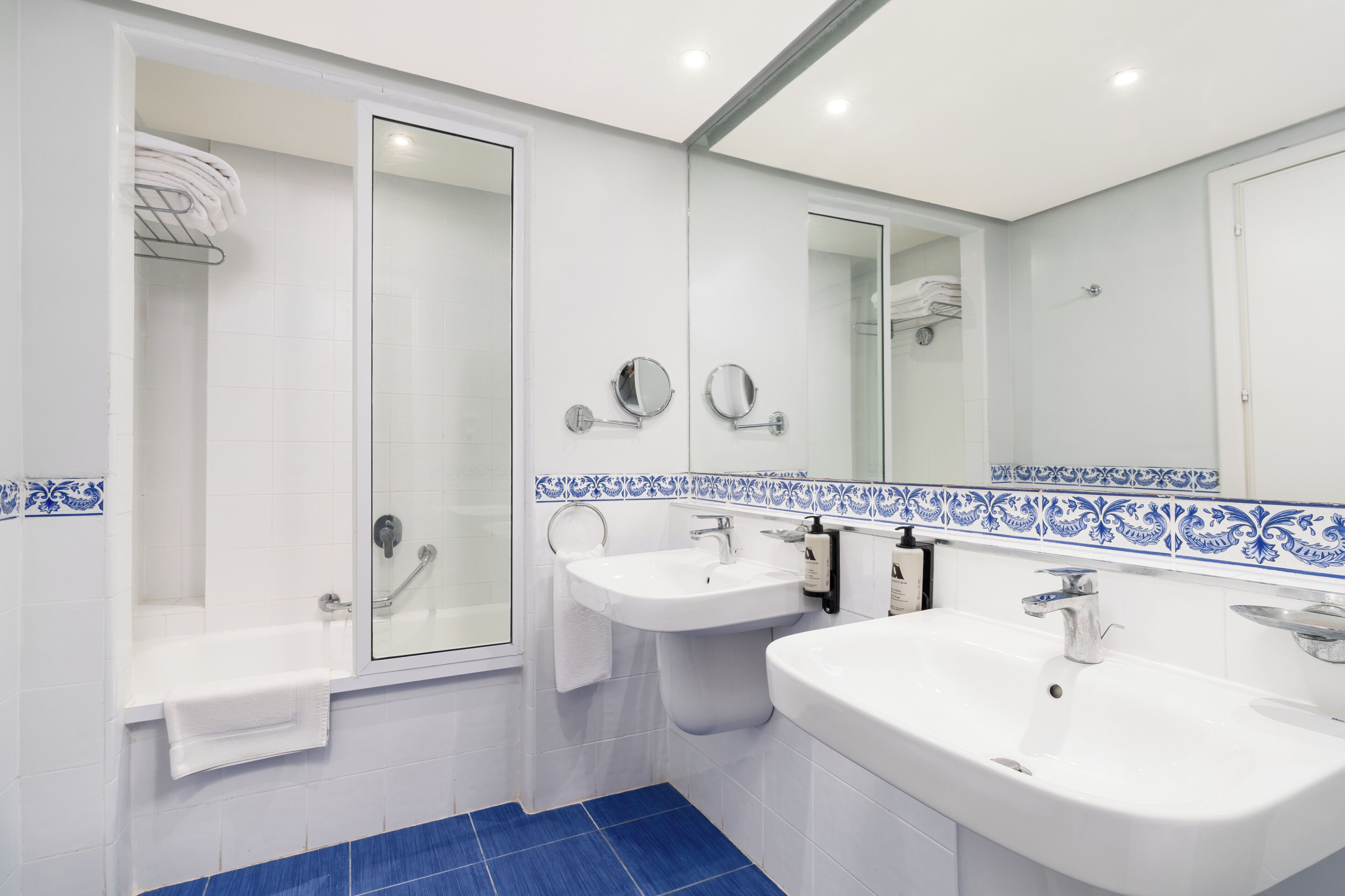 A modern bathroom with two sinks, a glass shower enclosure, and a large mirror.