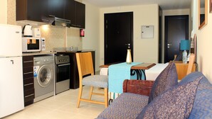 A compact living space with a kitchenette, a washing machine, a dining area with a table and chairs, and a sofa.