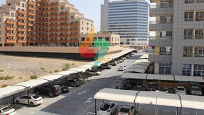 A multi-story parking structure with cars parked under covered areas, adjacent to a row of residential buildings.