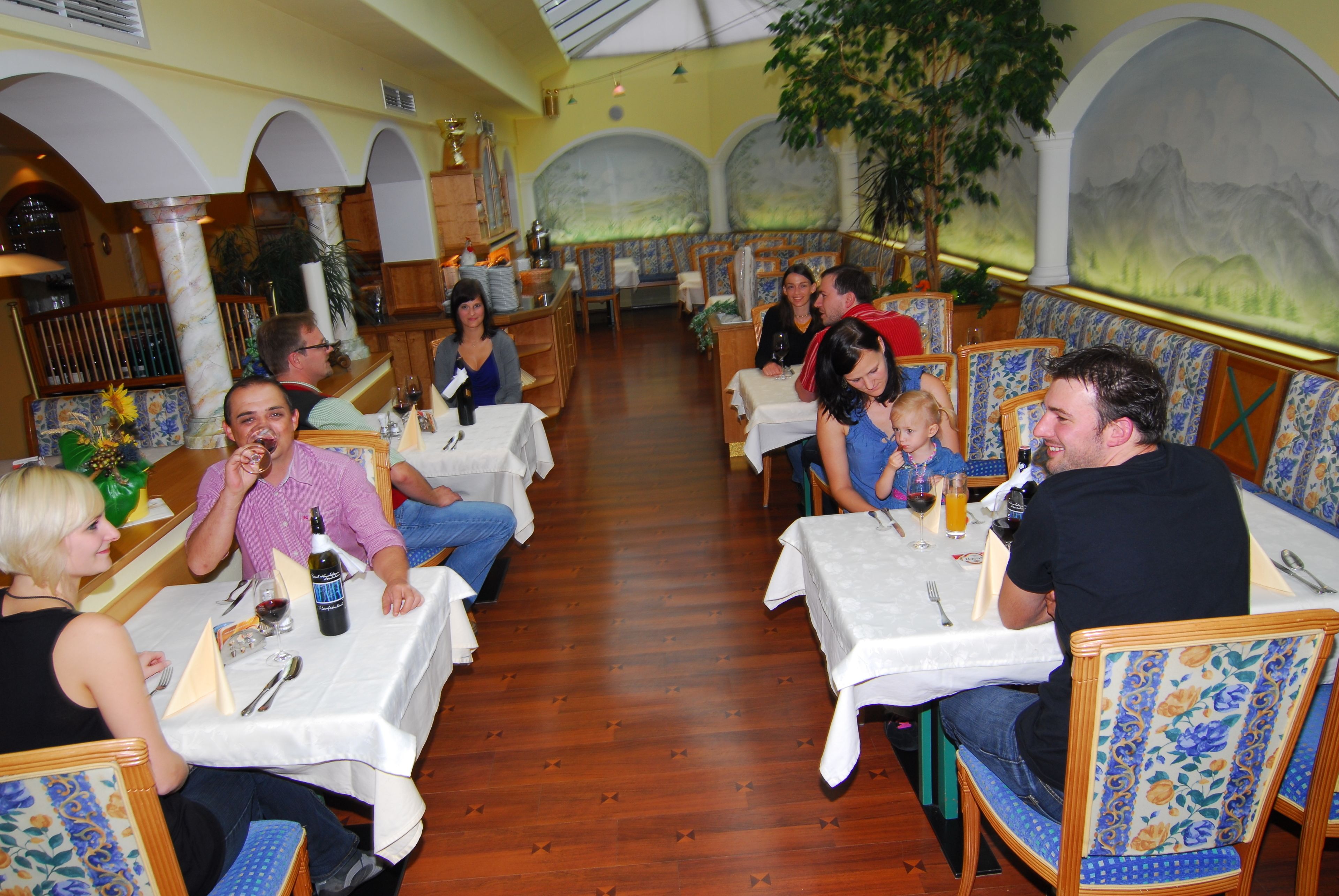 A restaurant with wooden floors, white tablecloths, and floral-patterned chairs.