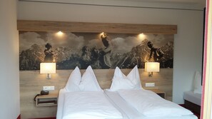 A hotel room with a large bed, two bedside lamps, a nightstand, and a wall mural of a mountainous landscape. - Hotel Lammertalerhof (Abtenau)