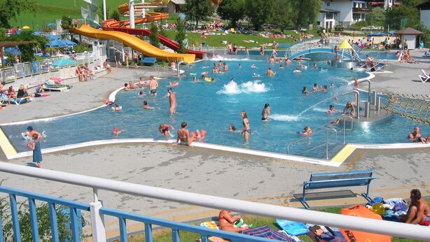 Zona de piscina con varias toboganes y una terraza rodeada de sillones de playa y sombrillas.