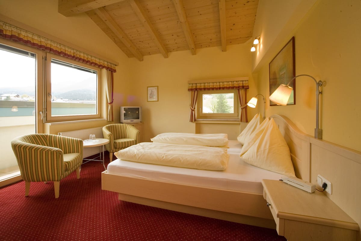 Habitación de hotel con cama, dos sillones, una mesita, televisor y grandes ventanales con vistas al mar.