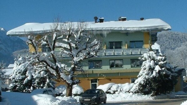 A multi-story building with a snow-covered roof and balconies, surrounded by snow-covered trees and a mountain in the background. - Hotel Lammertalerhof (Abtenau)