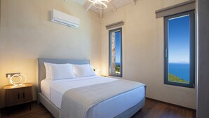 A bedroom with a bed, bedside tables, an air conditioner, and a window with a view.