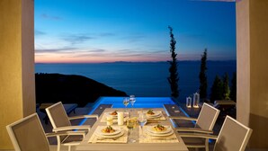 A dining table set for two with a view of the sea at dusk.