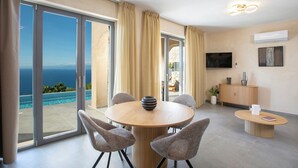 A modern room with a round table, chairs, a TV, and a view of the ocean.