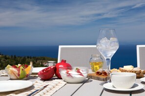 A table with a fruit salad, a bowl of yogurt, a glass of water, a martini glass, and a bottle of olive oil. - Ionian Horizon Villas (Lefkada)