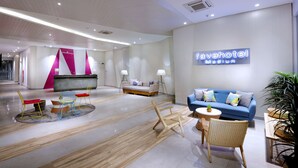 Un moderno vestíbulo de hotel con mostrador de recepción, sofás, sillas y una gran planta en maceta.