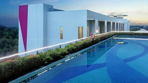 Un edificio moderno con piscina, un muro de acento rosa y vistas a la ciudad.