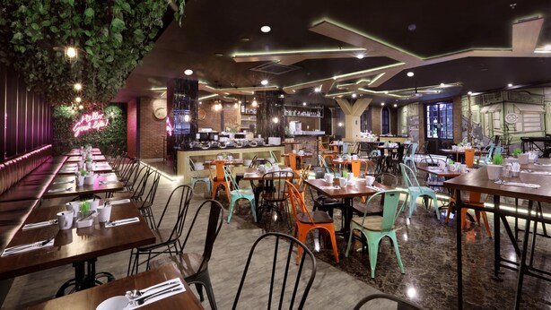 Un restaurante con mesas largas comunitarias, sillas coloridas y un letrero de neón.