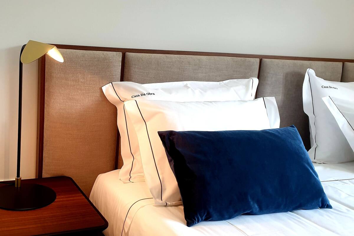 Ein ordentlich bezogenes Bett mit weißen und blauen Kissen, einer Nachttischlampe und einem Holennachttisch.