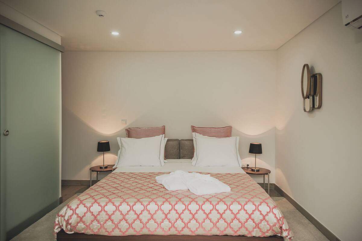 Ein Hotelzimmer mit einem großen Bett, zwei Nachttischen mit Lampen, einem Wandspiegel und einer Tür.