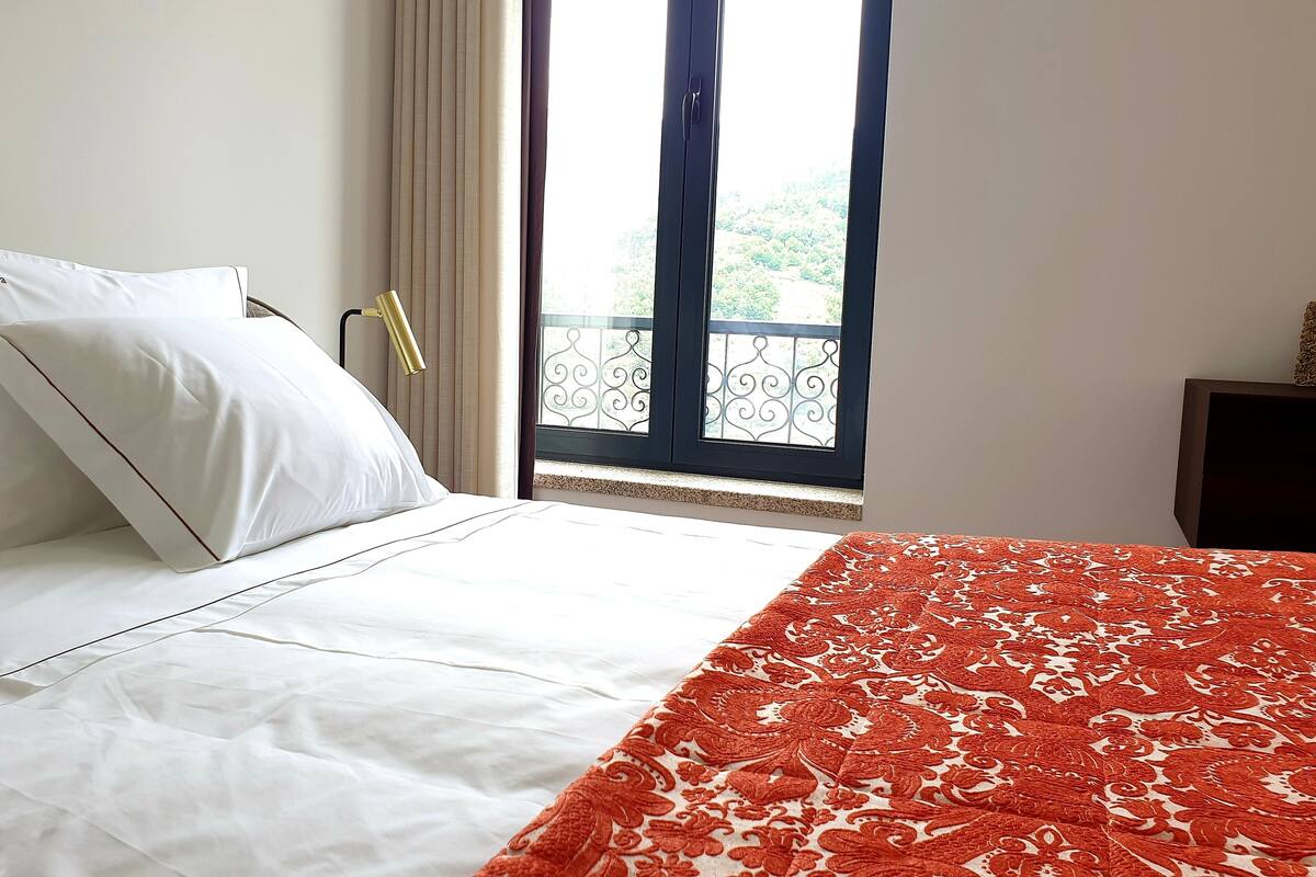 Ein Hotelzimmer mit einem Bett, einem Fenster mit Blick auf Grünflächen und einer gemusterten Tagesdecke.