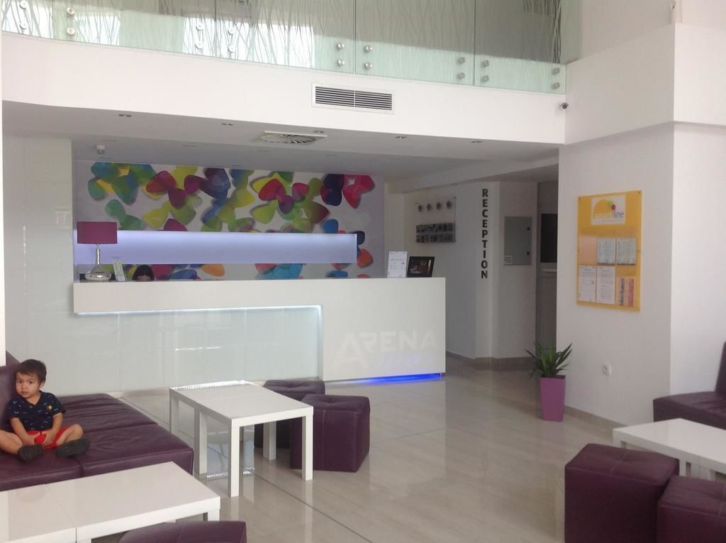 Un área de recepción moderna con un cuadro abstracto y colorido en la pared, una mesa de recepción y arreglos de asientos.