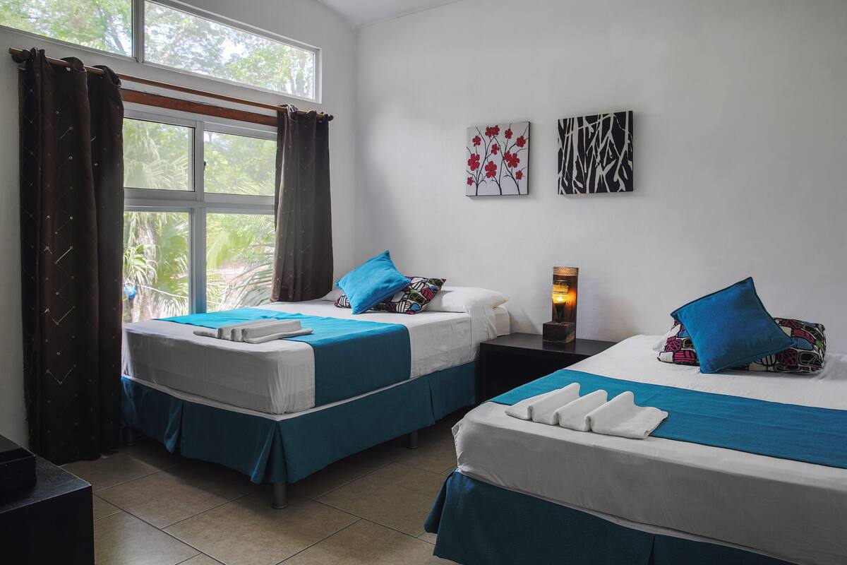 A hotel room with two beds, a window with curtains, and artwork on the wall.