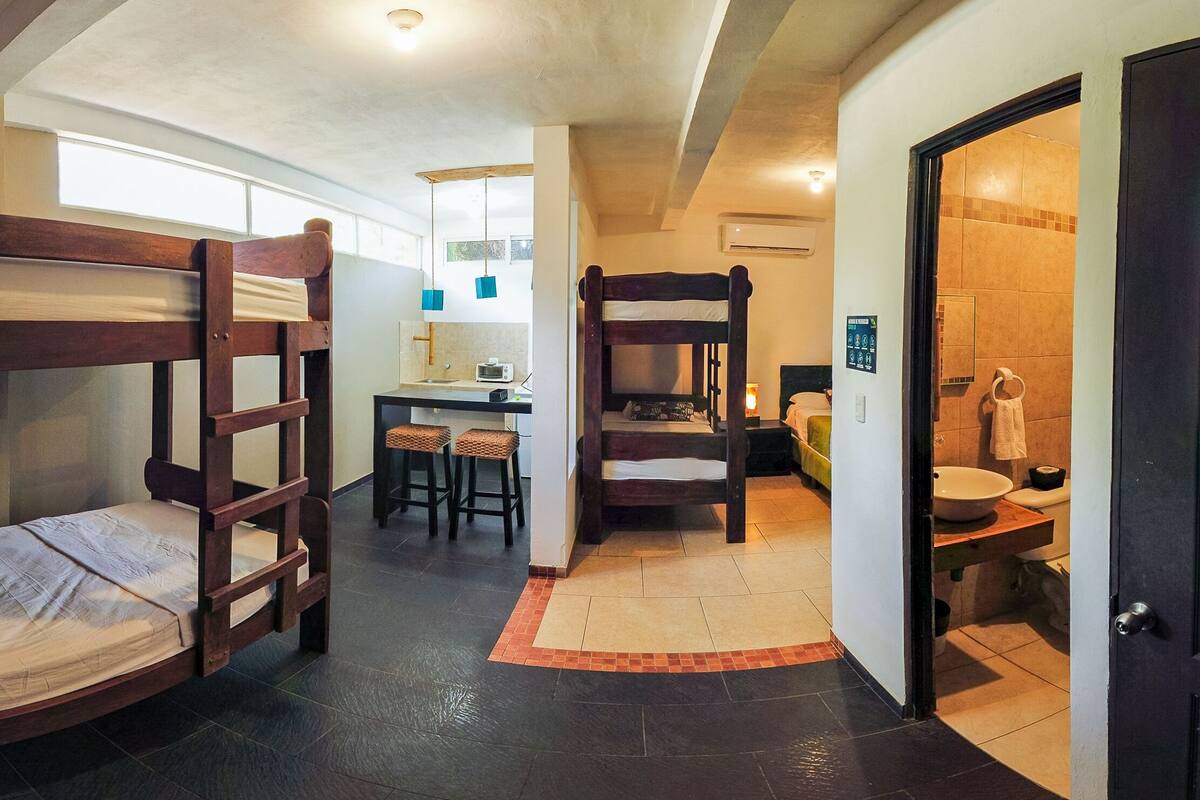 A dormitory room with bunk beds, a desk, chairs, and a bathroom with a sink and toilet.