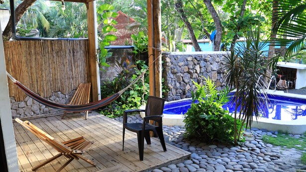 Una terraza de madera con una hamaca, una silla negra y un muro de piedra.