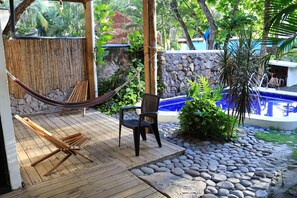 Una terraza de madera con una hamaca, una silla negra y un muro de piedra.