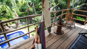 Una terraza de madera con una hamaca, piscina y una silla de madera.