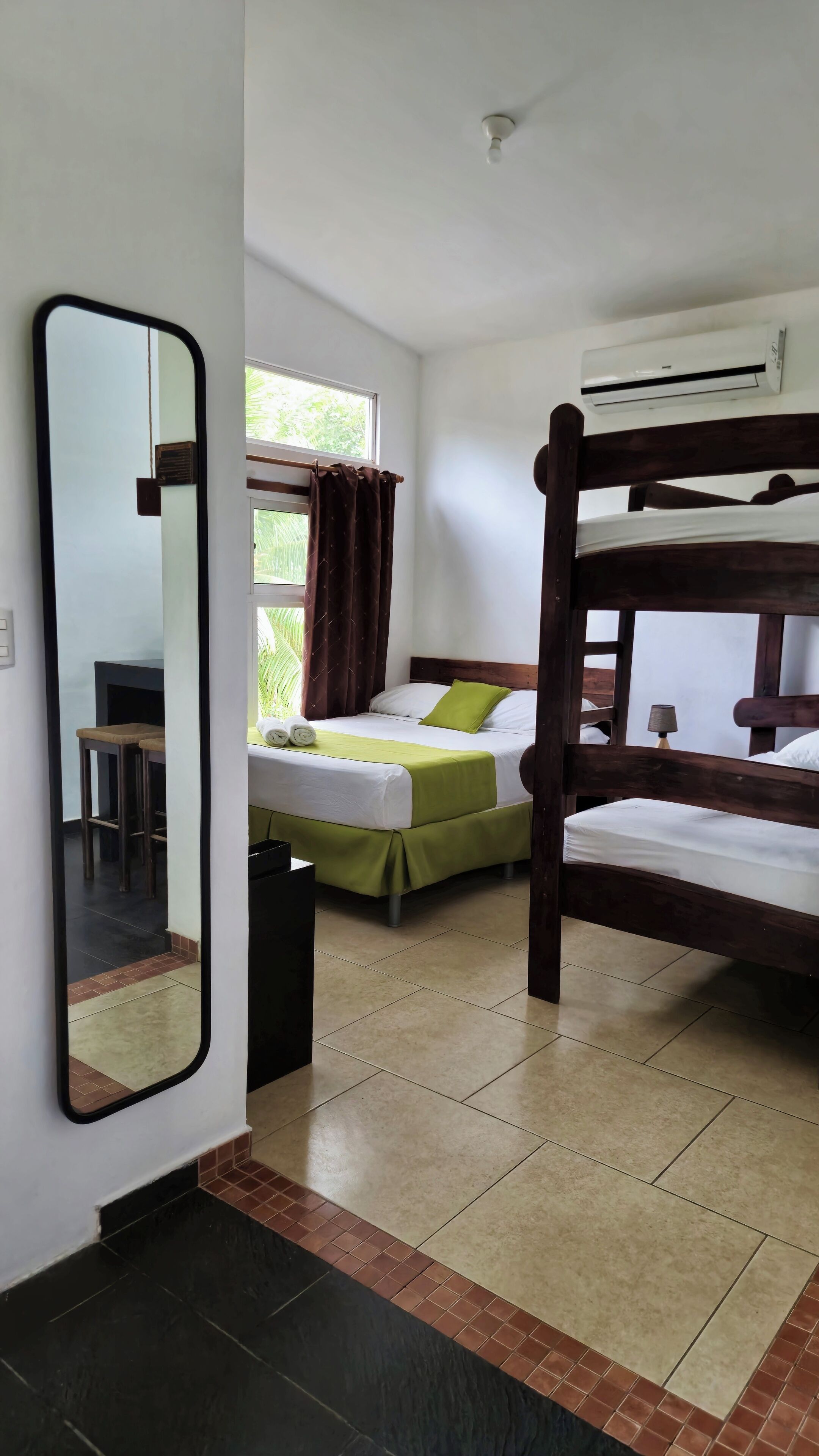 Una camera d'albergo con un letto a castello, una scrivania con una sedia, uno specchio e una finestra con tende.