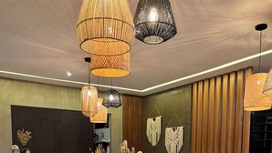 Un restaurante con mesas y sillas de madera redonda, lámparas de mimbre colgantes y tapices de macramé en las paredes.
