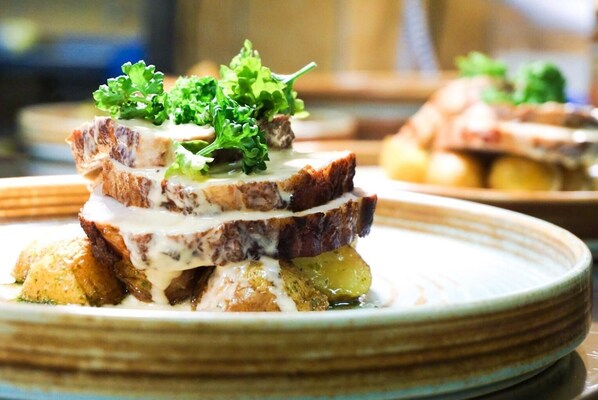 A dish with layered bread, meat, and a creamy sauce, garnished with greens, served on a plate.