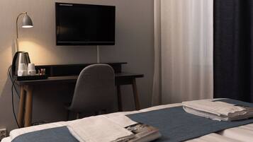 Habitación de hotel con cama, escritorio con computadora y lámpara, televisor y ventana con cortinas.