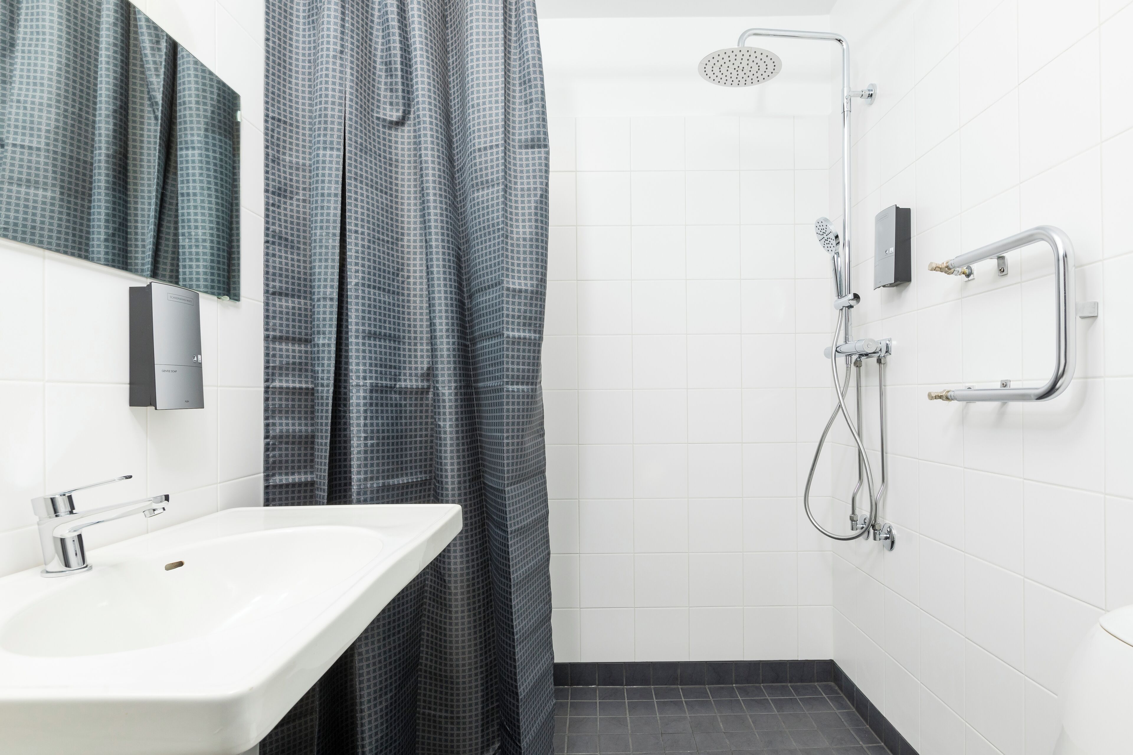 Ein modernes Badezimmer mit einem weißen Waschbecken, einer Dusche mit Duschbrausehandstück und einem Handtuchhalter.