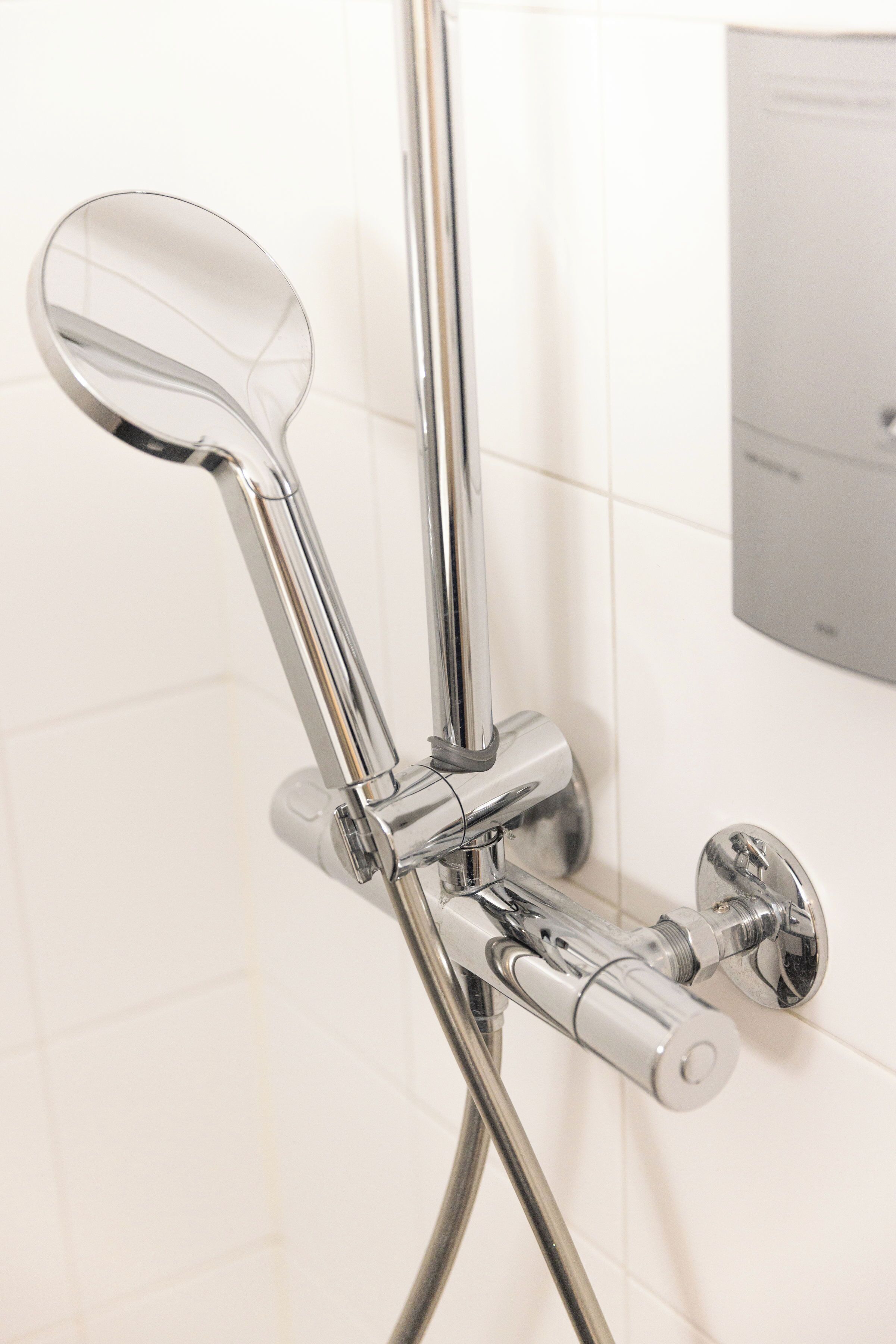 A chrome showerhead with a handheld mirror attached to a wall-mounted faucet.
