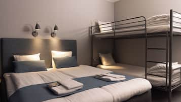 Una habitación de hotel con una cama grande, una cama individual y una litera. Hay luces fijadas a la pared y un cabecero.