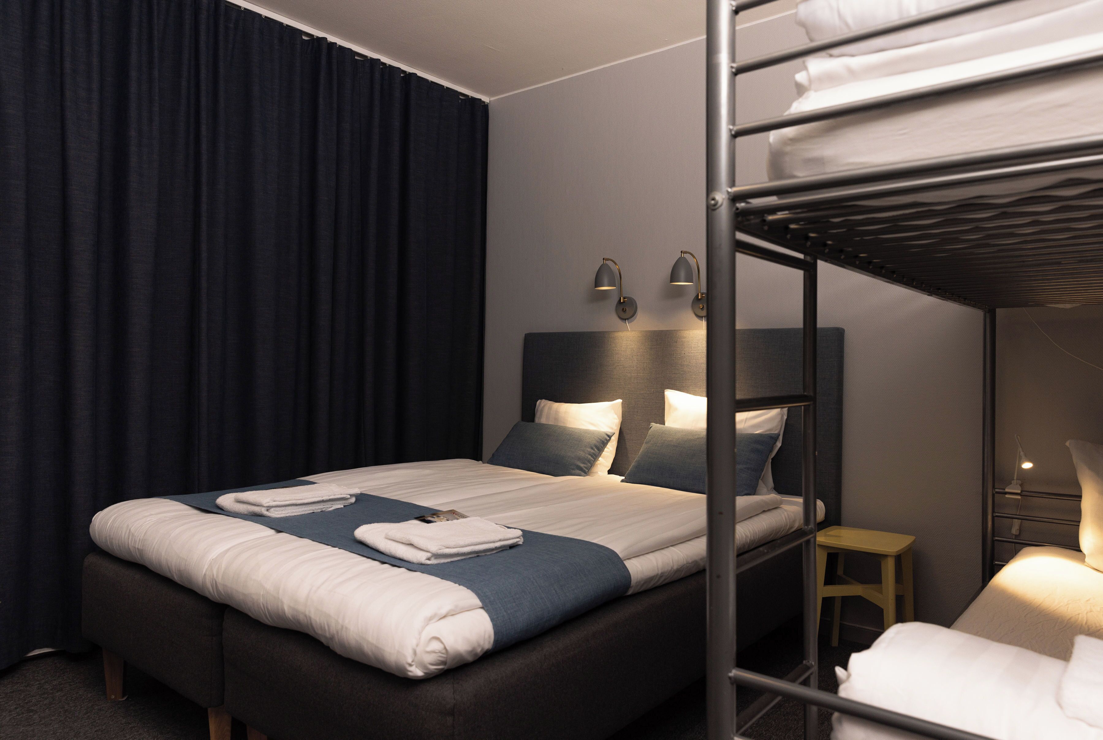 A hotel room with a bunk bed, a single bed, a bedside table, and a lamp.
