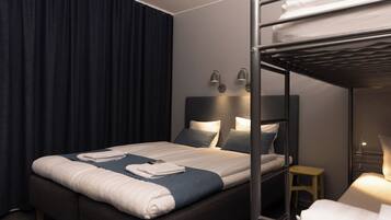 A hotel room with a bunk bed, a single bed, a bedside table, and a lamp.