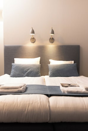 Una cama bien hecha con dos almohadas, una toalla doblada y una revista encima.