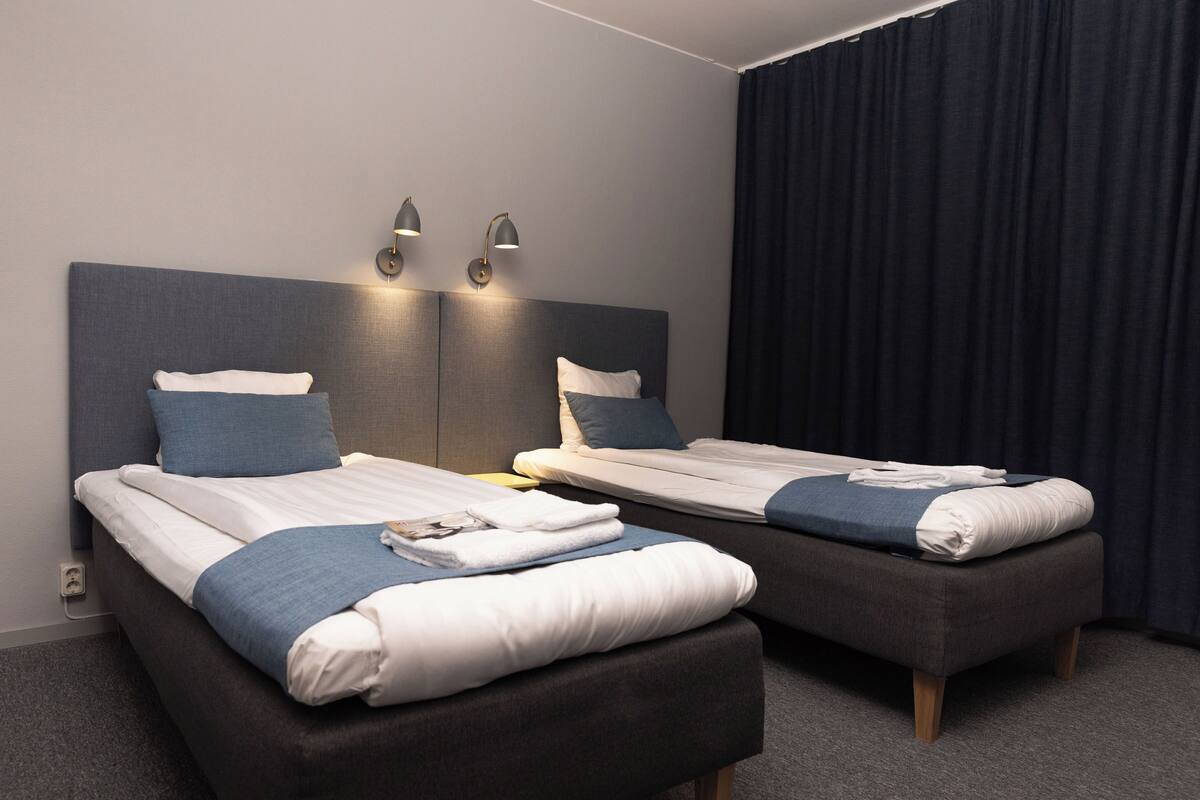 A hotel room with two beds, a dark curtain, and wall-mounted lights.