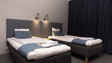 A hotel room with two beds, a dark curtain, and wall-mounted lights.