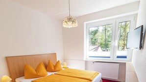 A hotel room with a bed, a desk, a chair, a window, and a television. - Hotel Waldidyll (Ostseebad Baabe)