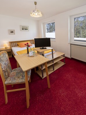 A hotel room with a bed, a desk with a computer, a chair, a red carpet, a window, and a ceiling light. - Hotel Waldidyll (Ostseebad Baabe)