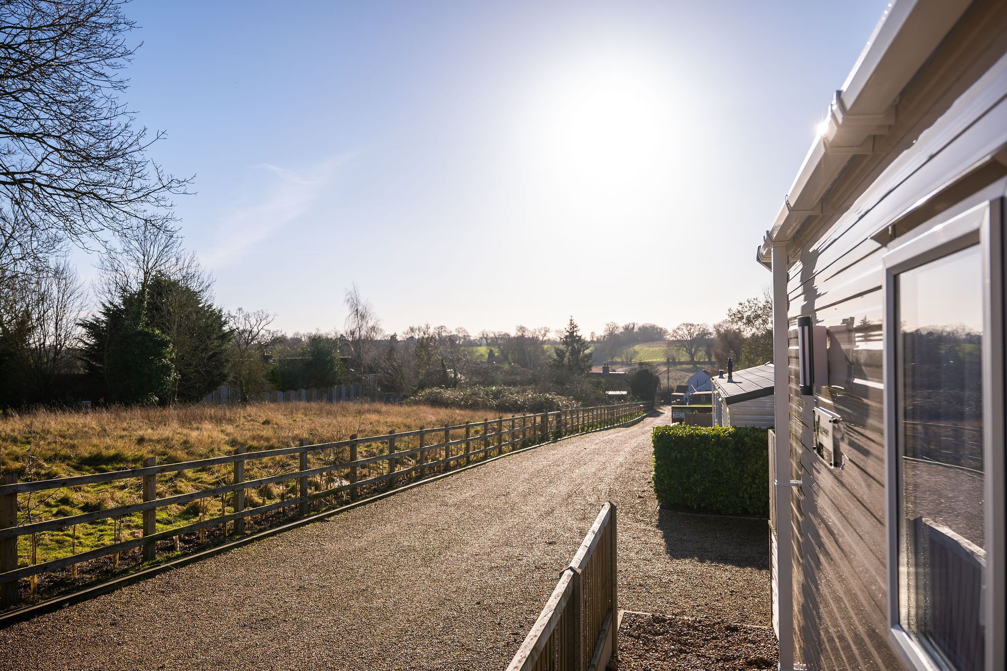 A gravel path leading to a building with a wooden fence and a hedge.
