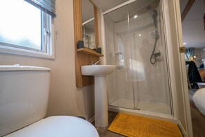 A bathroom with a toilet, sink, and glass-enclosed shower. - The Travellers Rest (Halesworth)