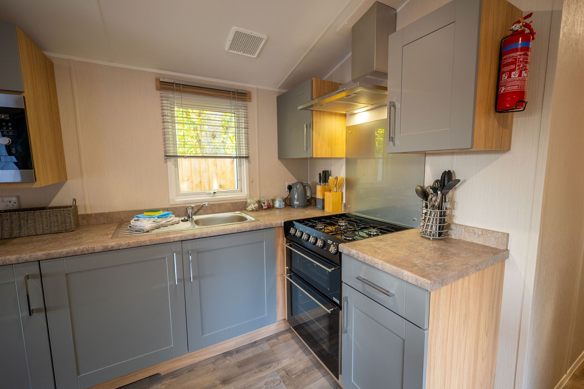A compact kitchen with grey cabinets, a gas stove, a sink, and a window with blinds.