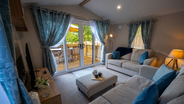 A cozy living room with a grey sofa, blue cushions, and a wooden side table with a vase and teapot. - The Travellers Rest (Halesworth)