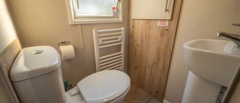 A compact bathroom with a toilet, a sink, a window, and a wooden wall.
